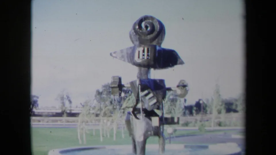 1969 Sacramento 8mm frame showing the abstract sculpture's spiral top and arm-like metal forms above lawn and fountain spray.