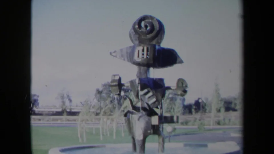 1969 Sacramento frame of the kinetic-looking metal fountain sculpture, with spiral top, dark panels, water spray, and landscaped grounds.