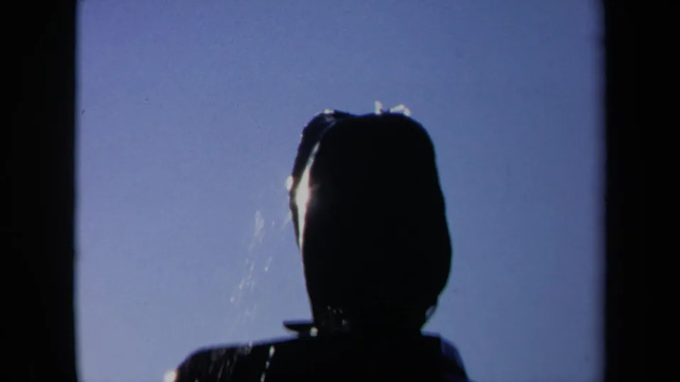 Tight 1969 Sacramento home-movie frame of the fountain's headlike upper shape, backlit with faint water streaks against blue sky.