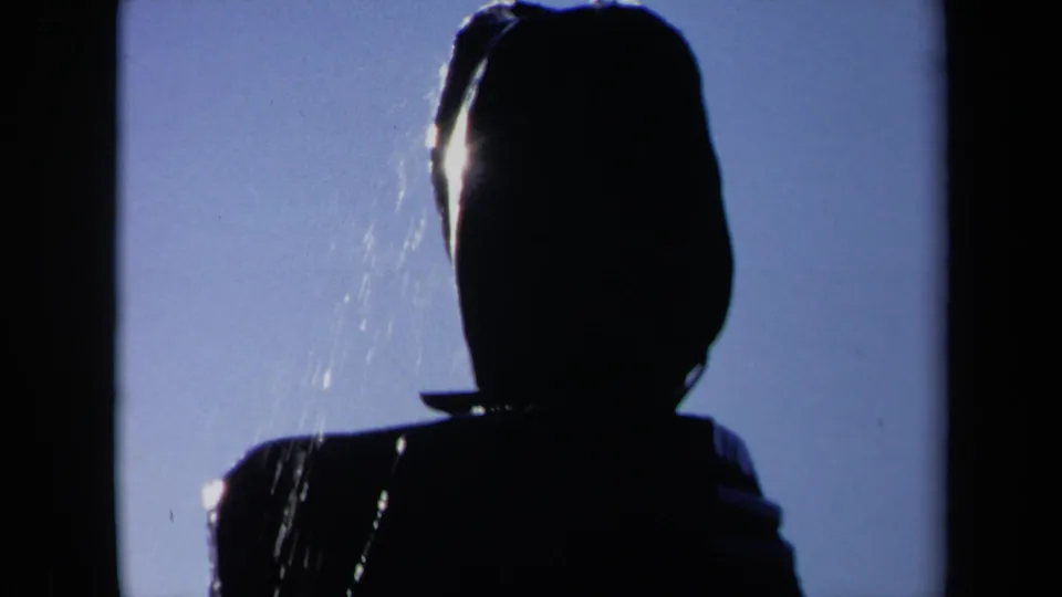 1969 Sacramento 8mm frame with a close dark silhouette of a head and shoulders, backlit by blue sky and crossed by falling water.