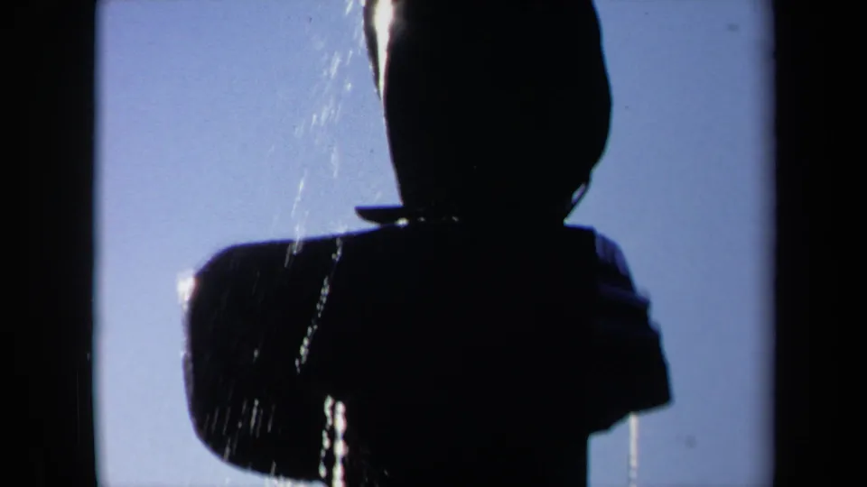 1969 Sacramento 8mm frame showing the silhouetted figure more fully, with water falling over the head and shoulder area against a clear sky.