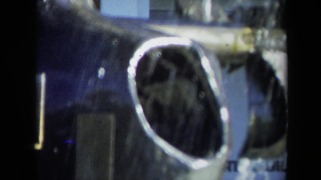 1969 Sacramento 8mm frame showing a reflective hollow metal piece, possibly aircraft-related, in soft focus.