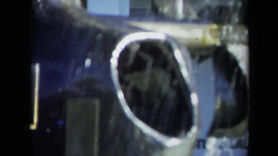 1969 Sacramento 8mm frame showing a reflective hollow metal piece, possibly aircraft-related, in soft focus.