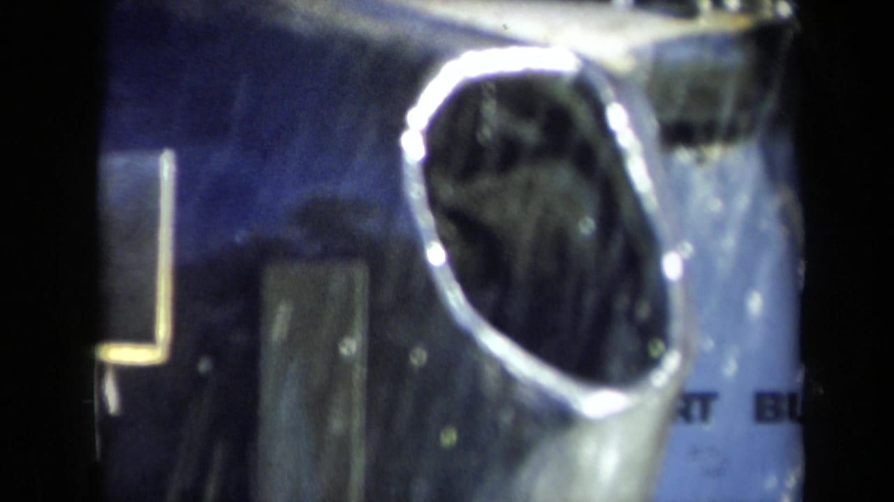 Reflective metal opening seen beside dark blue machinery and film-frame borders.