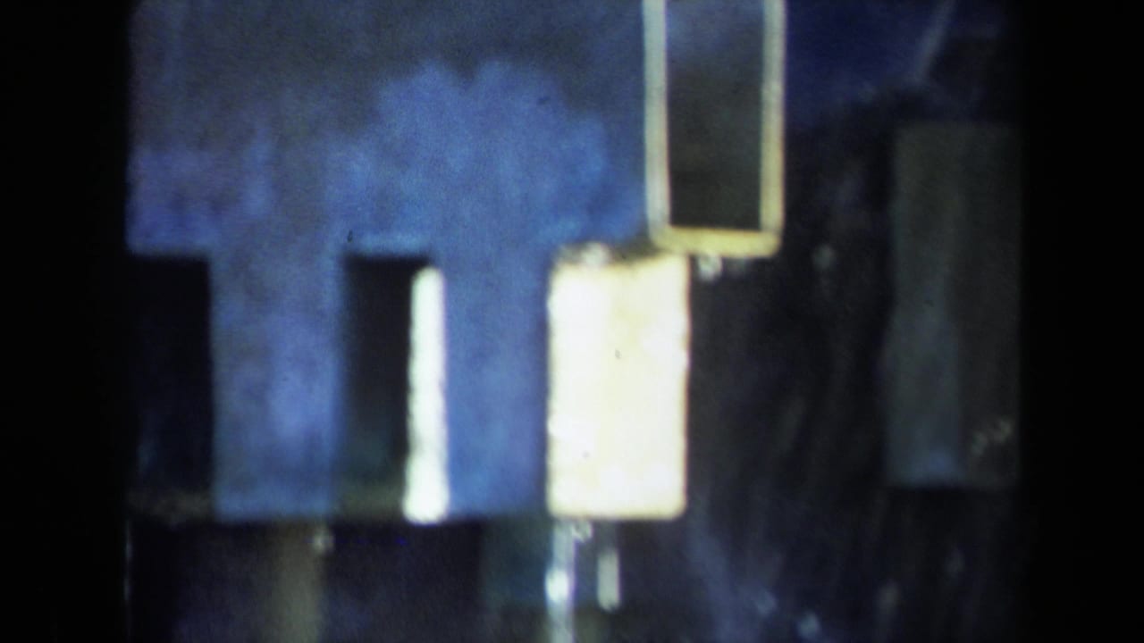 1969 Sacramento 8mm frame showing dark industrial machinery surfaces, vertical forms, and bright reflected panels in soft focus.