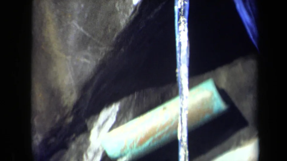 1969 8mm frame from Sacramento metadata showing a vertical water stream beside a turquoise pipe or rail and dark wet surfaces.