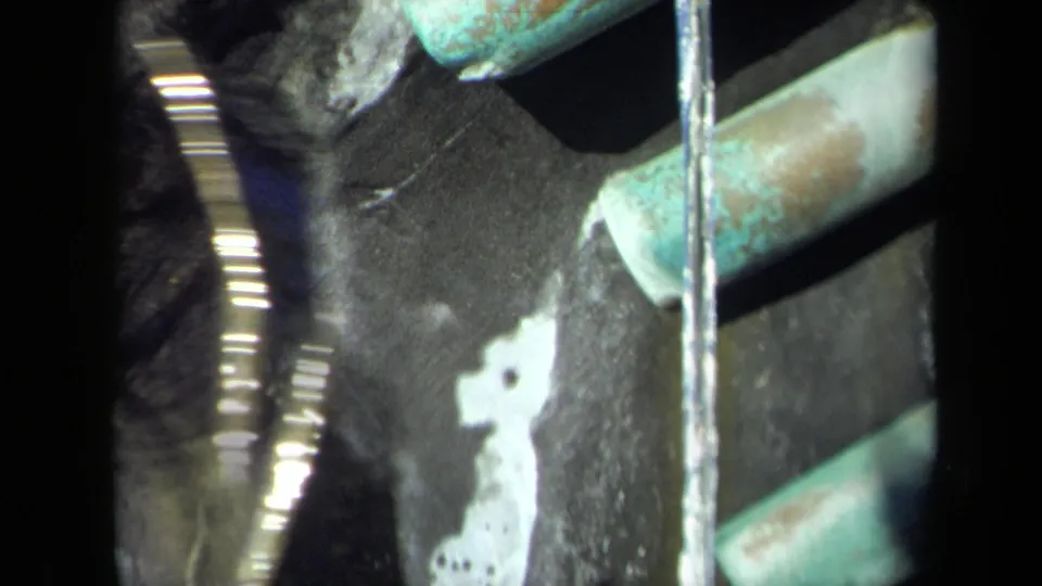 1969 8mm frame showing a vertical water stream, turquoise pipe or rail, and bright splash traces on a dark surface.