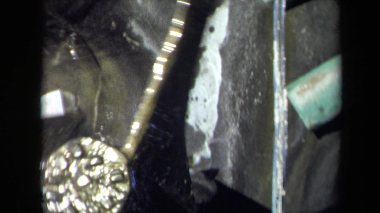 Close view of a gold-toned rotating wheel beside dark wet metal and flowing water.