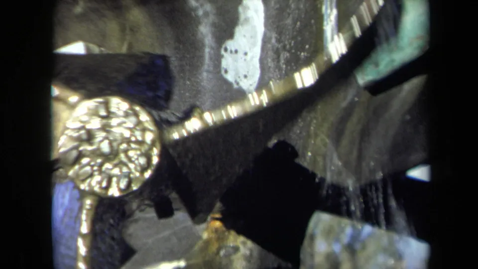 Close 8mm frame of the Sacramento mill mechanism, with a gold-colored rotating part, dark supports, and water splashing nearby.