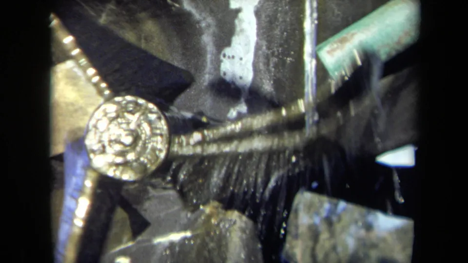 1969 8mm close-up of the mill mechanism with the gold-toned wheel lower in frame, water crossing the dark metal assembly.