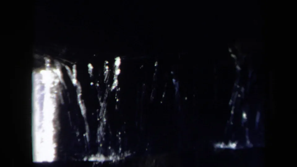 Shadowed 1969 8mm close-up of water moving across glossy black metal parts within the mill mechanism.
