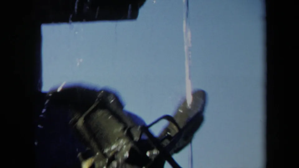 1969 home-movie still showing the lower portion of a dark wet propeller with water trailing down against bright sky.