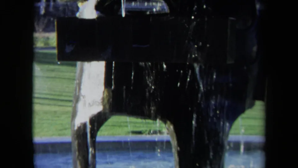 1969 Sacramento 8mm frame showing a close view of a dark fountain with water streaming down near a pool and lawn.