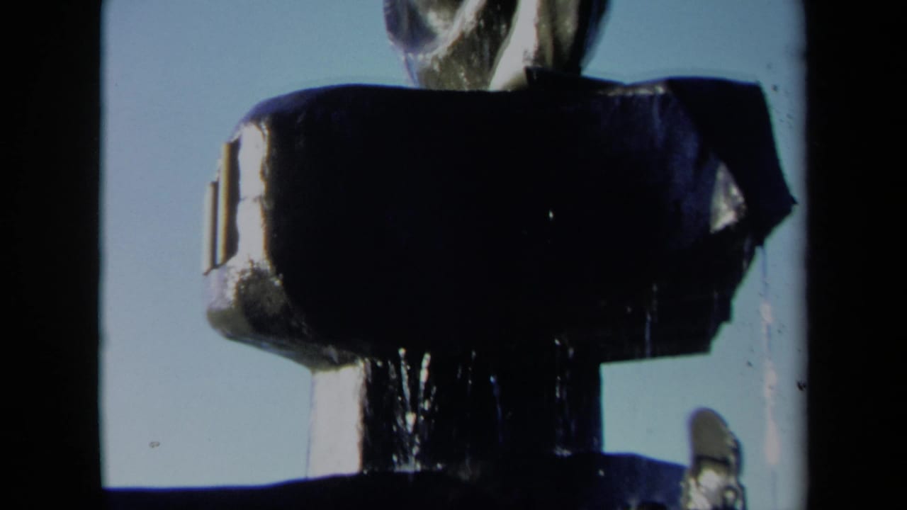 Close view of a dark fountain basin with water falling below a spiral sculptural form.