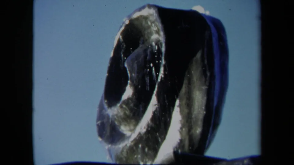Close 1969 Sacramento 8mm view of a dark coiled fountain sculpture with water shine and a blue sky background.