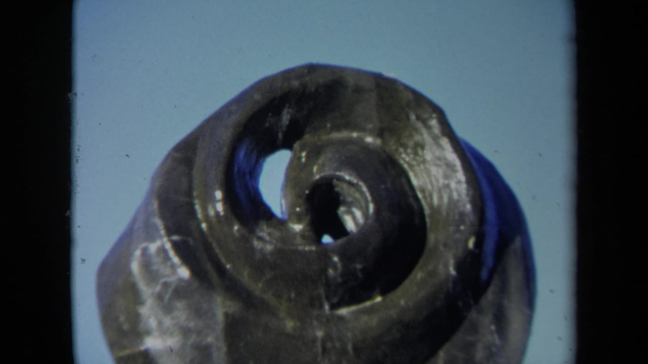 Close view of a dark bronze spiral fountain form with two central openings against a pale blue background.
