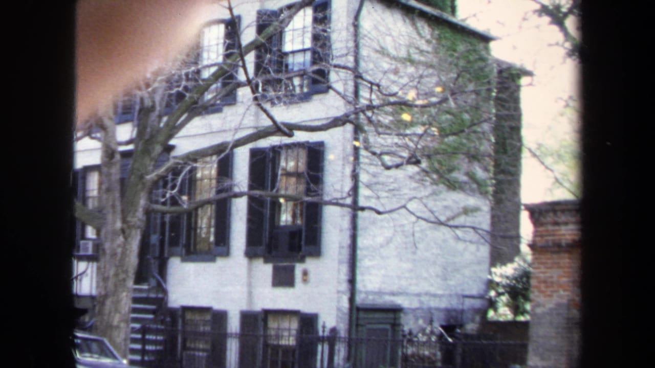 White brick townhouse with black shutters seen through a dark window frame.