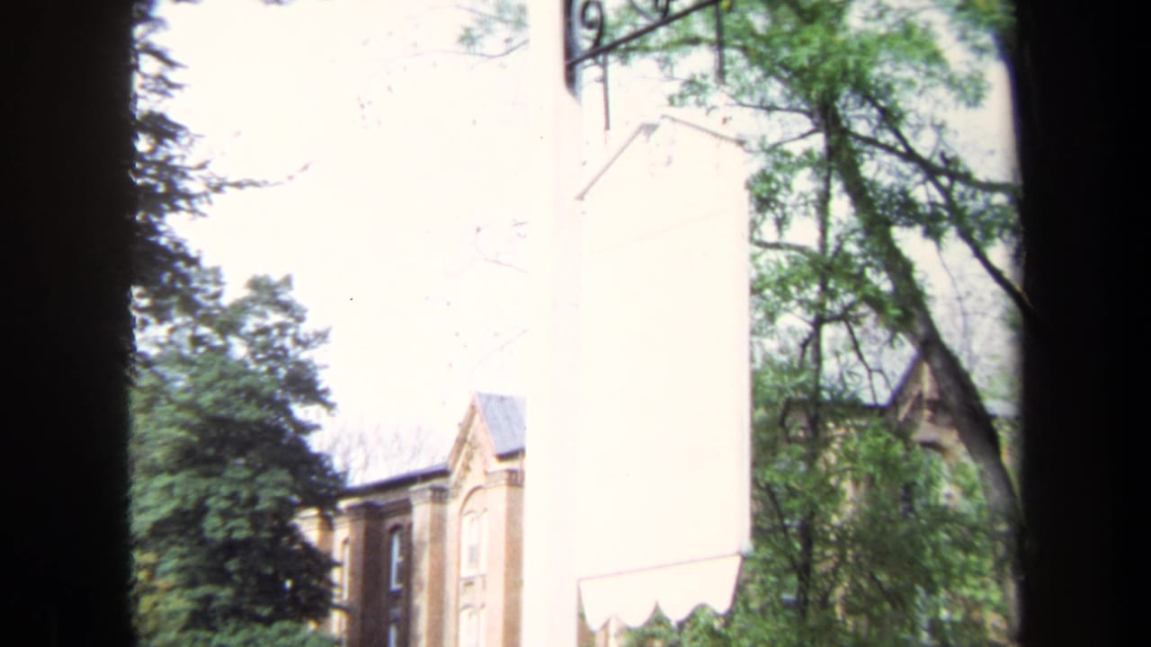 Brick building and trees partly blocked by a dark vertical frame and pale wall.