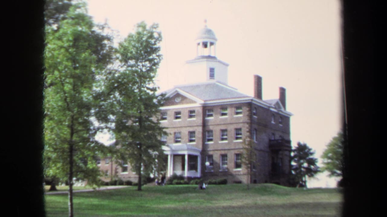 Brick building with cupola and white entrance columns behind trees on a lawn.