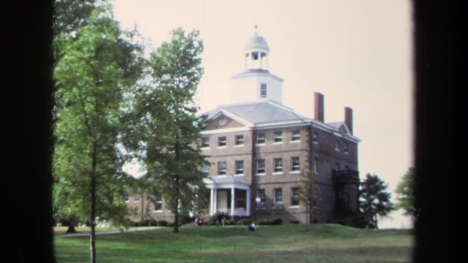 1970 8mm frame of the Annapolis building from the lawn, with the cupola and portico partly framed by trees and film-edge borders.