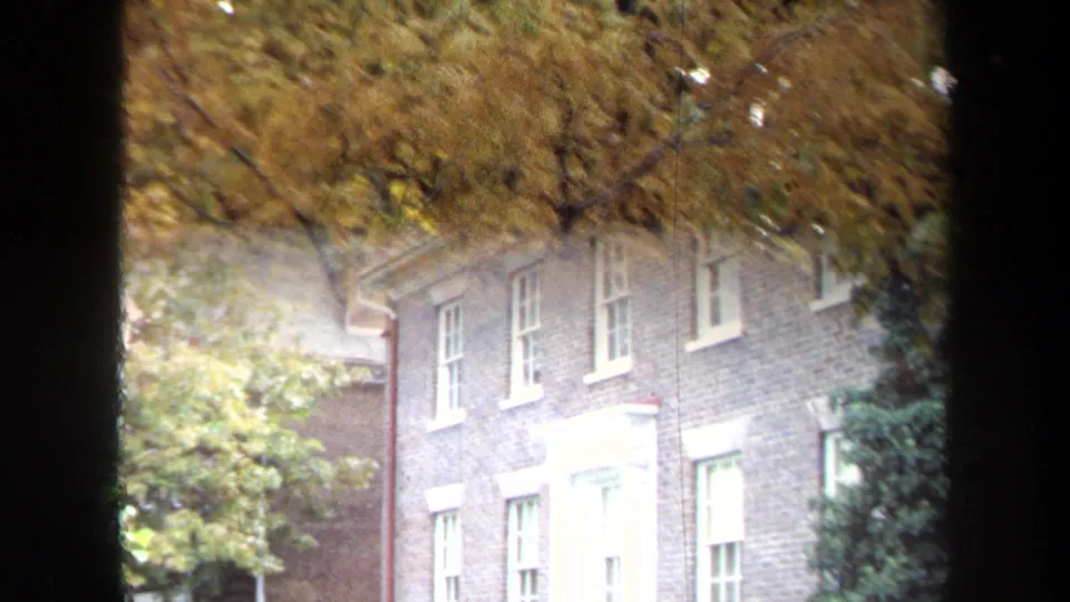 A brick building with white-trimmed windows appears behind autumn branches in 1970 Annapolis home-movie footage.