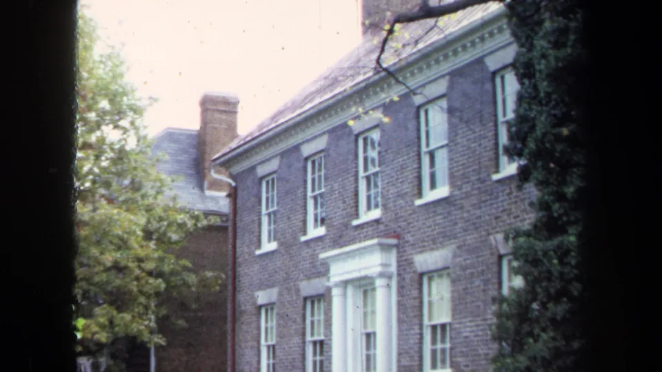 Two-story brick building in Annapolis with white sash windows, a columned entrance, shrubs, and trees, captured on 8mm in 1970.