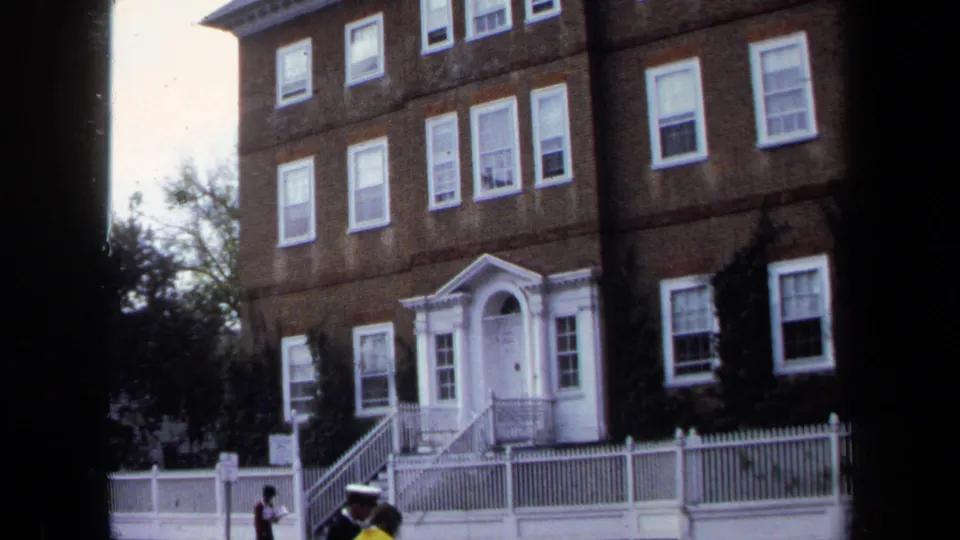 1970 Annapolis frame showing a multi-story brick building with a white portico, front fence and small people near the steps.