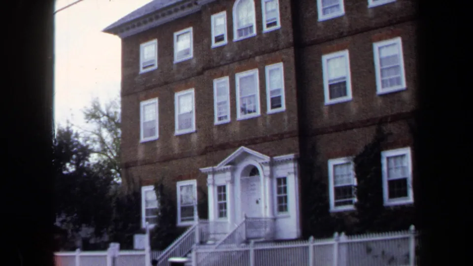 1970 Annapolis 8mm frame showing a large brick building with white-trimmed windows, a formal doorway, and a white fence.