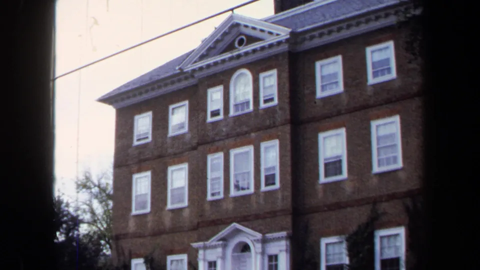 1970 Annapolis 8mm frame with a slightly tilted view of the brick building, white-trimmed windows, doorway, and fence.