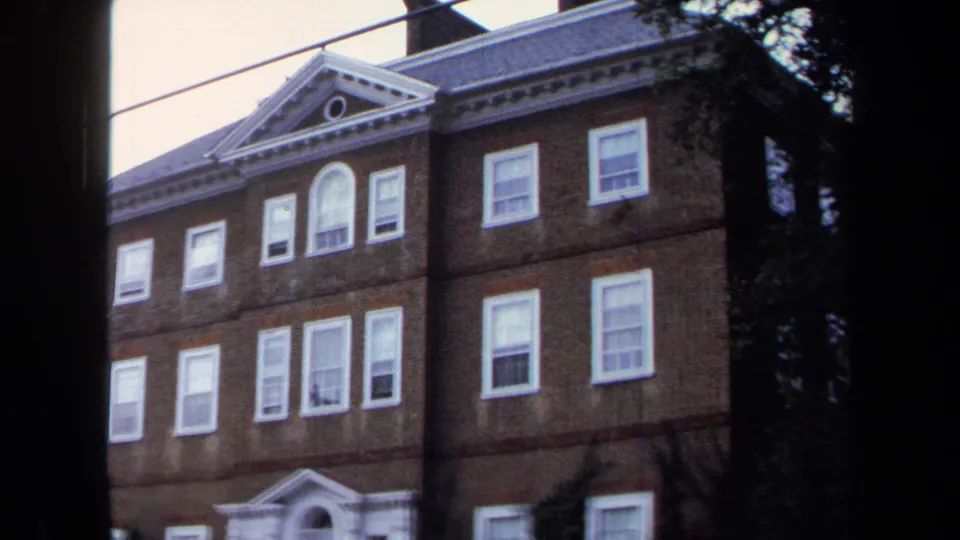 1970 Annapolis frame showing the brick building facade, classical roofline, white windows, entrance area, and trees at the edge.