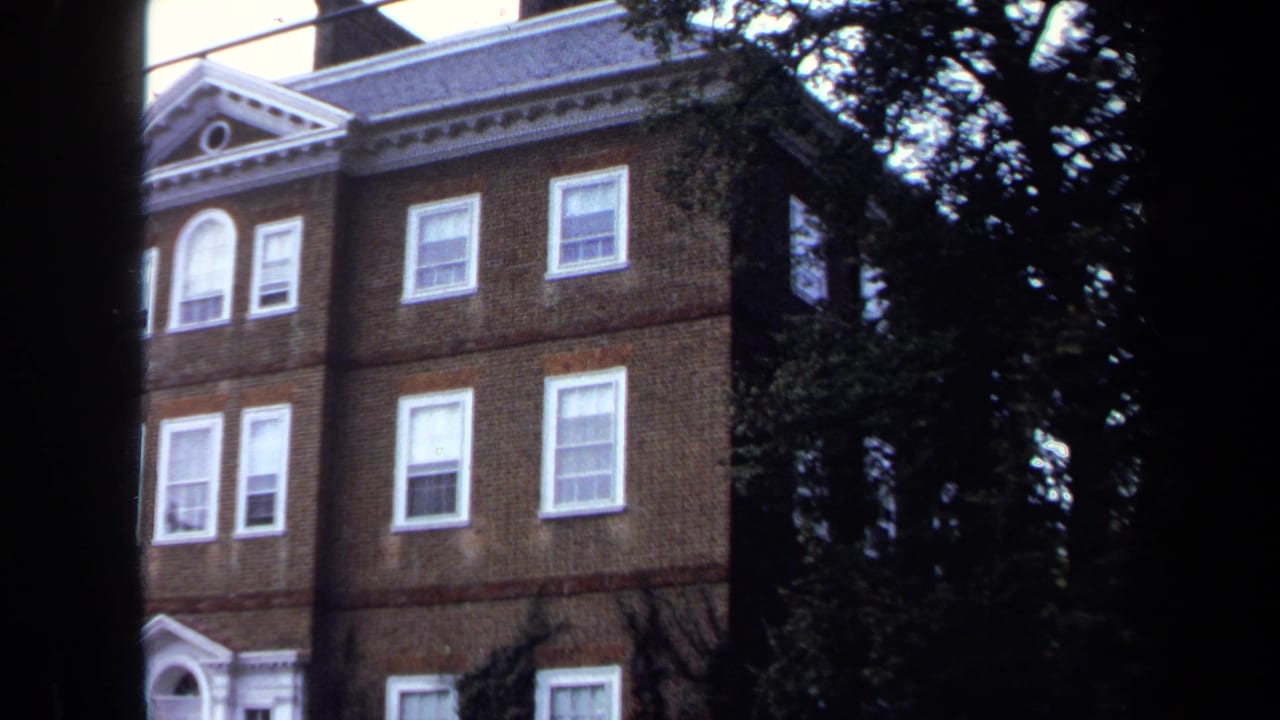 1970 Annapolis view of a brick building's upper stories, with white trim, sash windows, roof pediment, and trees partly obscuring the frame.