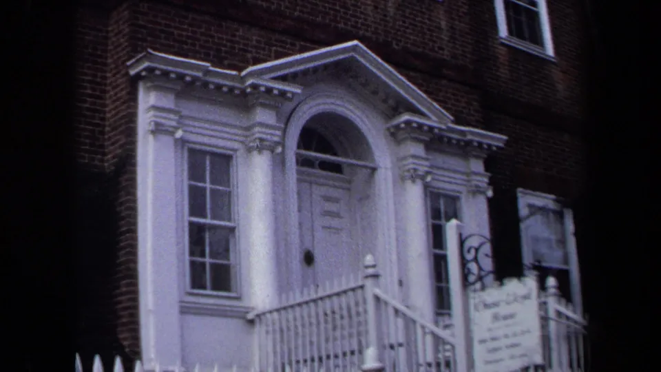 1970 Annapolis 8mm close view of the building entrance, showing white columns, an arched doorway, railings, brickwork, windows, and a partially readable sign.