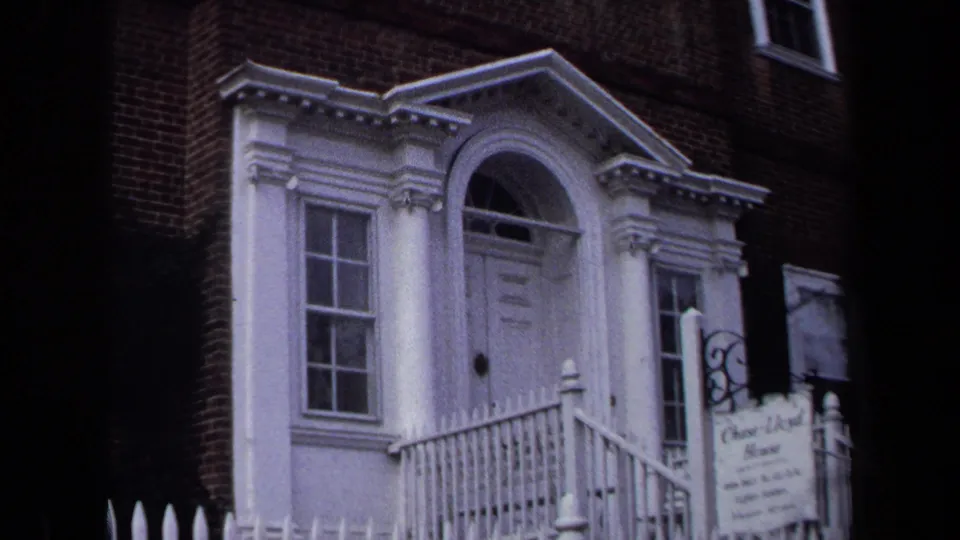 1970 Annapolis 8mm frame showing the Chase Lloyd House entrance with white columns, arched doorway, railings, and hanging sign.