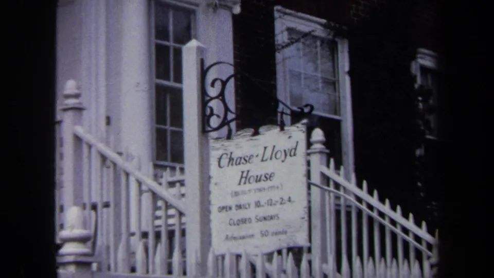 Close 8mm frame of the Chase Lloyd House sign with partial hours and admission text visible near the entrance railing.