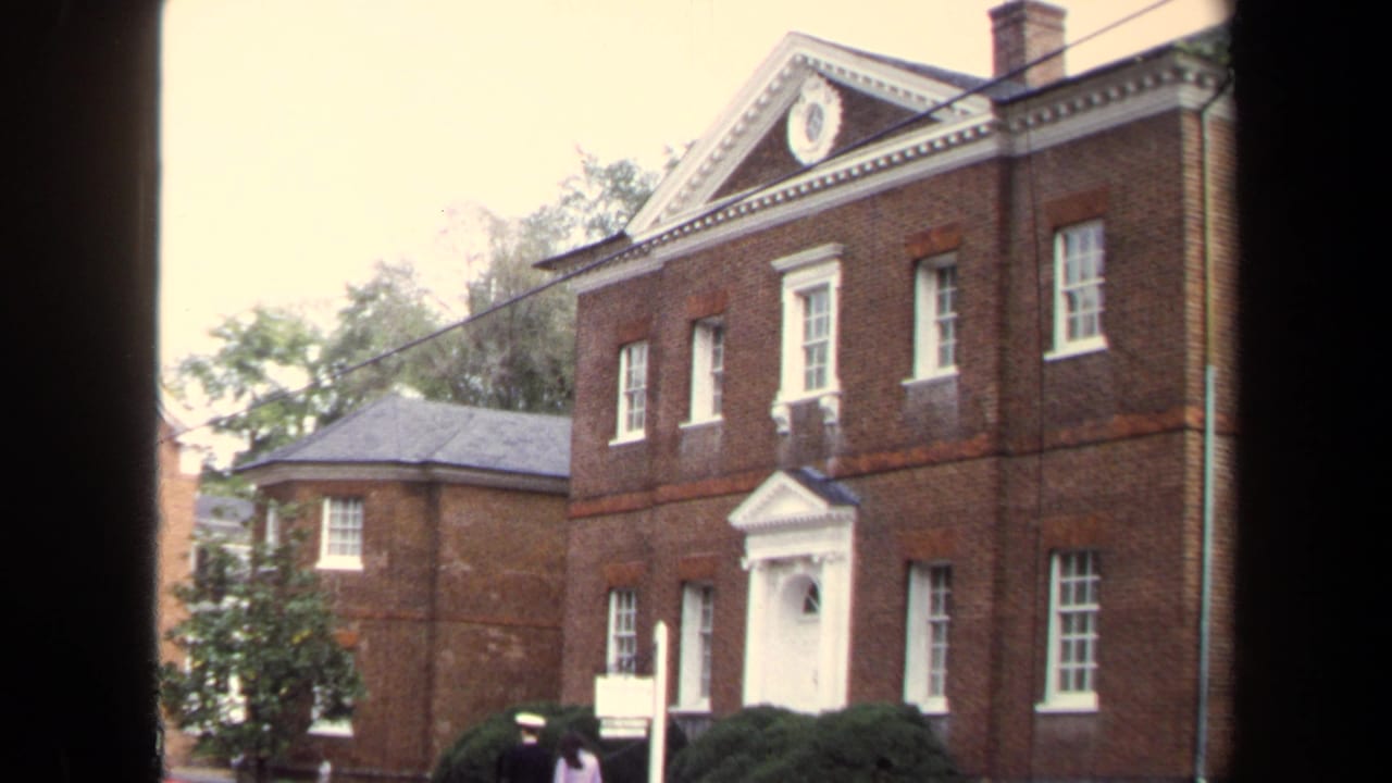 Red brick historic house with white doorway, shrubs, and visitors near the entrance.