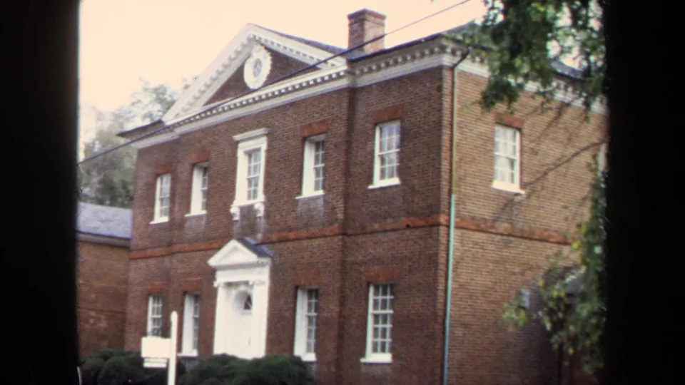 1970 Annapolis view of the Chase-Lloyd House facade and side wall, with white windows, shrubs, tree branches, and dark 8mm frame edge.