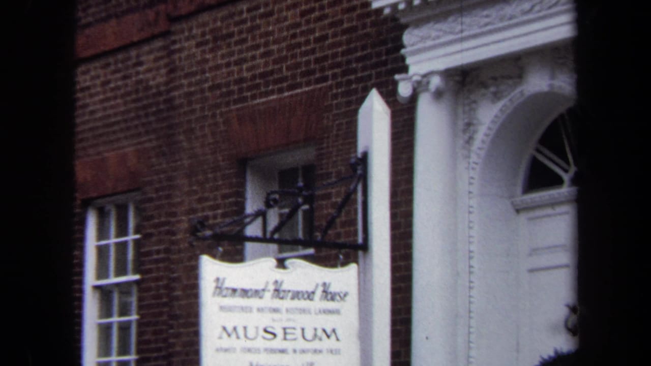 Brick museum facade with hanging sign beside a white classical doorway.