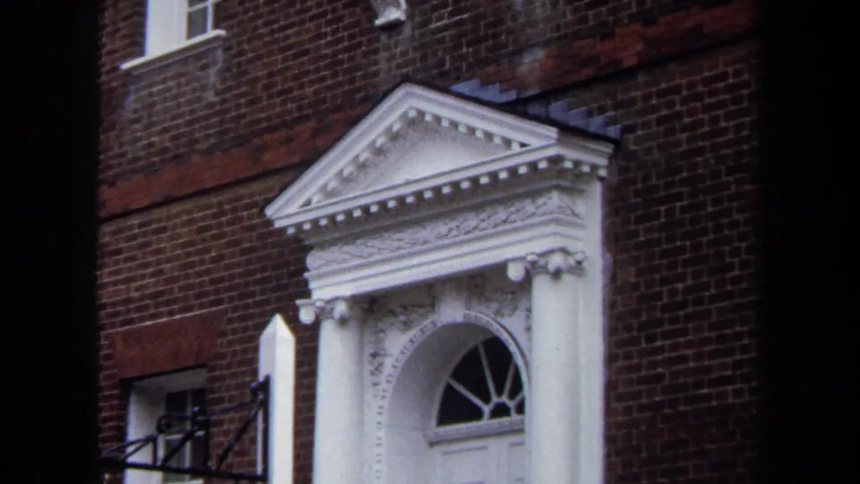 Handheld 8mm view of the Hammond-Harwood House doorway in Annapolis, with white columns, pediment, fanlight, and brick facade.