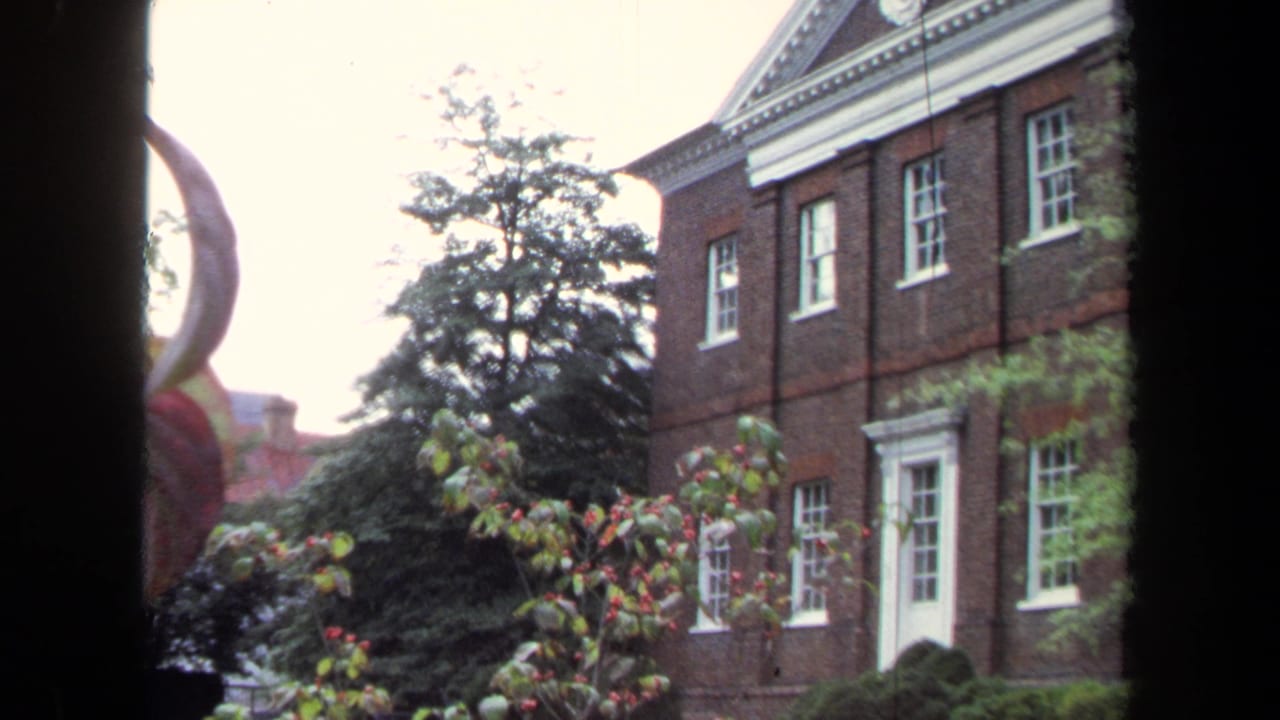 1970 Annapolis 8mm frame showing a historic-looking brick facade, white-trimmed windows, greenery, and dark framing from a nearby window.