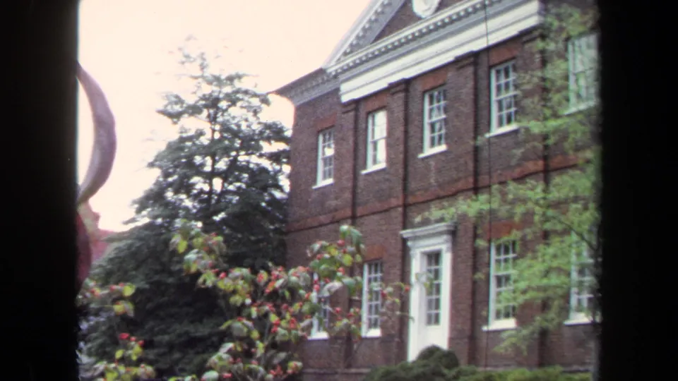 1970 Annapolis view of a brick historic-style building partly obscured by trees and dark vertical foreground window framing.