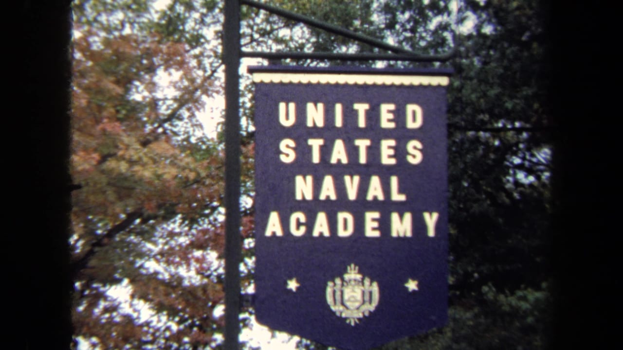 1970 Annapolis 8mm frame showing a United States Naval Academy banner with white lettering, trees, and dark film-frame edges.