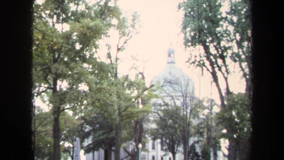 1970 Annapolis 8mm view of a white domed Naval Academy building partly hidden by trees and bright sky.