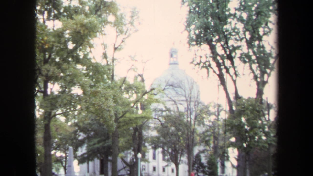1970 Annapolis home-movie view of a distant domed civic building seen through trees and dark frame edges.