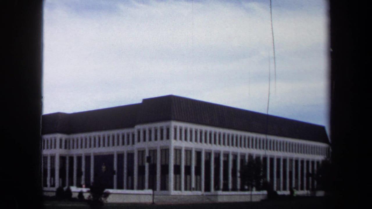 White-columned institutional building seen across a lawn under a cloudy sky.