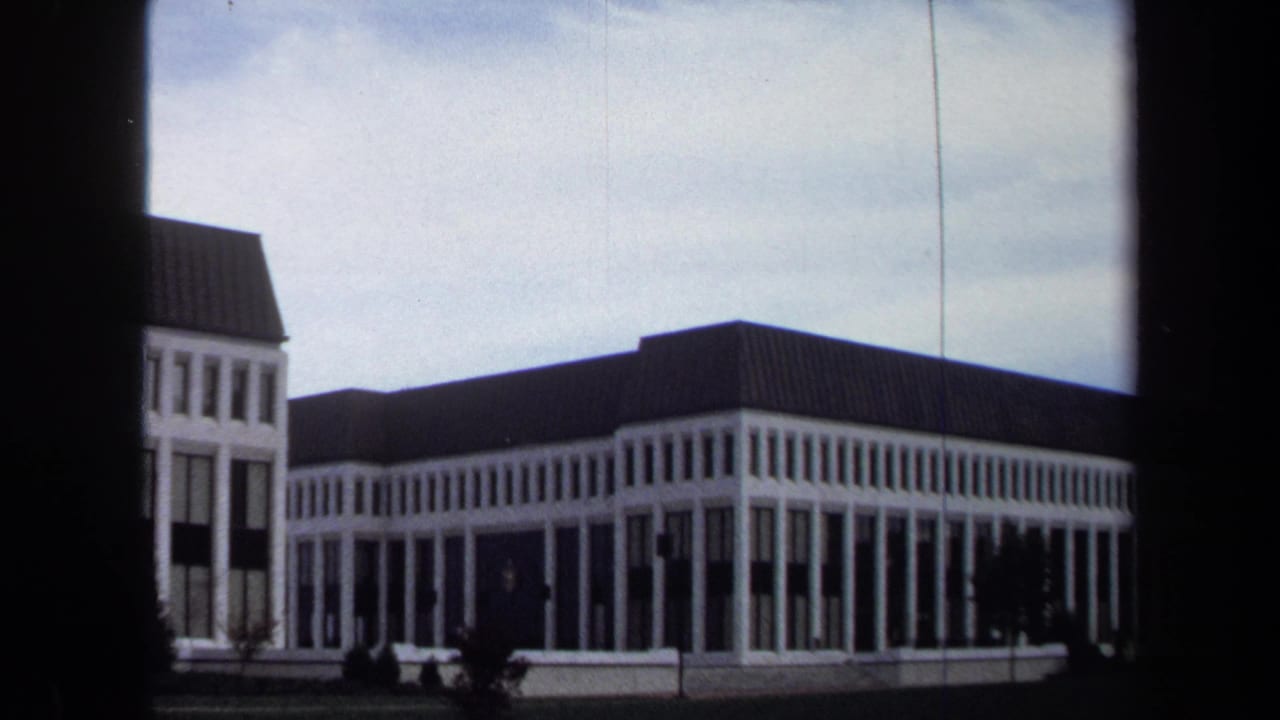 1970 Annapolis frame of a large formal building across a manicured lawn, partly framed by dark film borders.