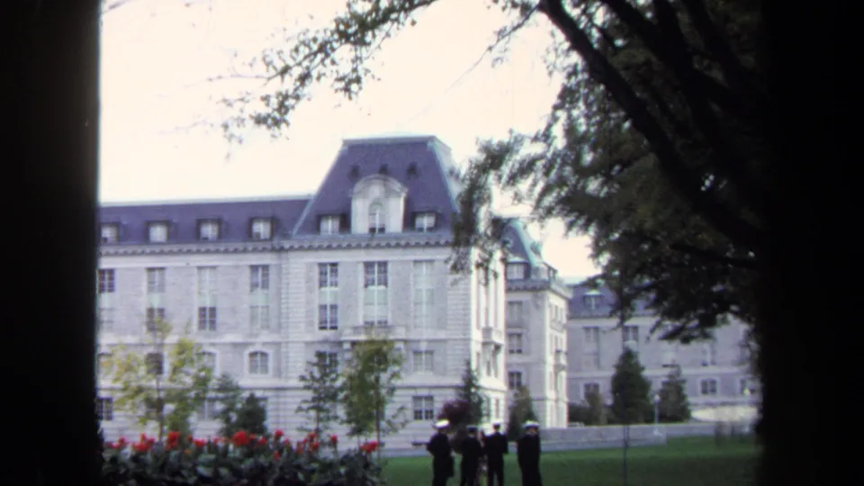1970 Annapolis home-movie view of a pale stone institutional building with cadets grouped at the edge of the lawn.