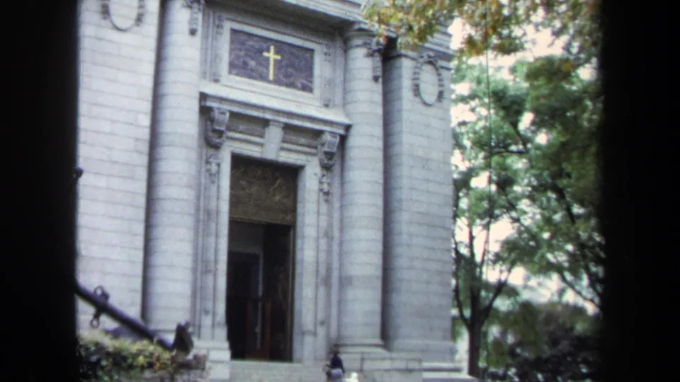 1970s Annapolis frame of the church entrance, with a gold cross over the door, stone columns, trees, and a partial anchor in front.