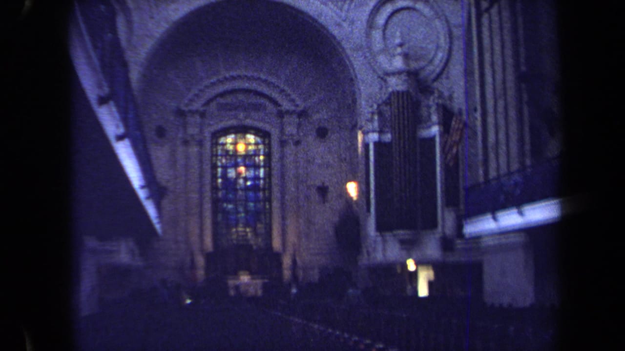1970 Annapolis 8mm frame showing a church interior with stained glass, carved stone archwork and organ pipes in low blue-toned light.