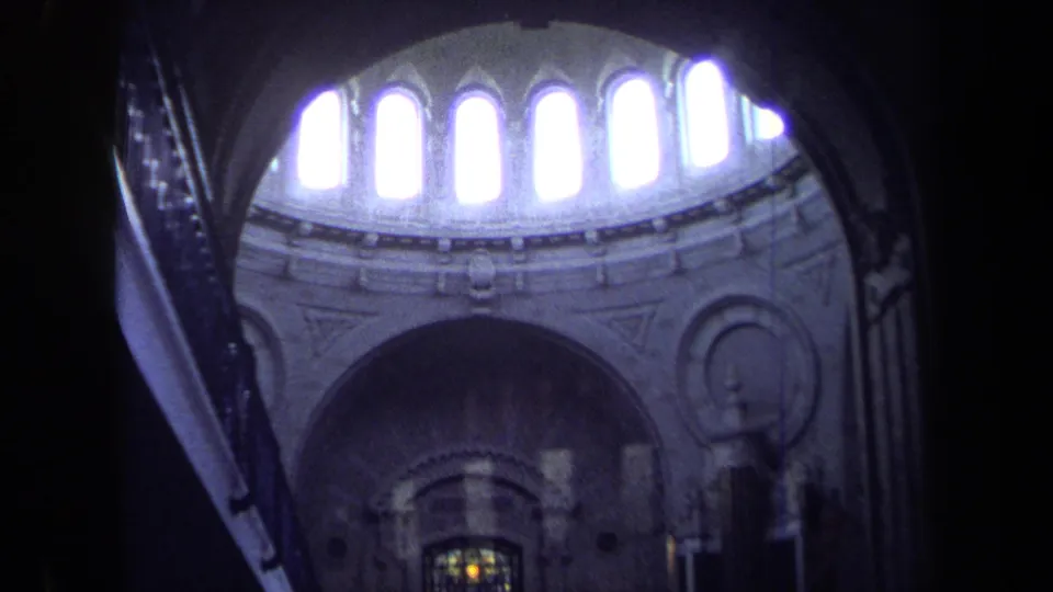 1970 Annapolis 8mm frame showing bright clerestory windows across a domed church ceiling with stained glass low in view.