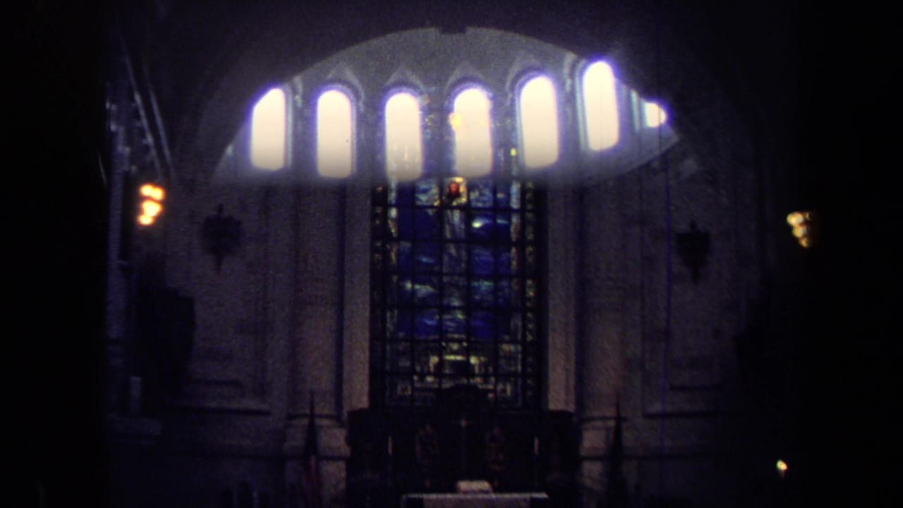 1970 Annapolis 8mm frame looking through an arched cathedral opening toward tall windows and a blue stained-glass panel in low light.